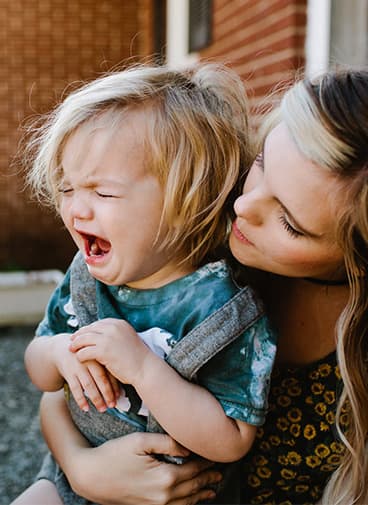 Young caucasian child crying in mother’s arms